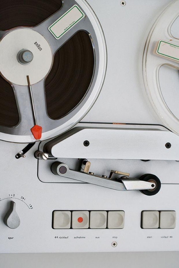 Close-crop of a white reel-to-reel deck, soft grey keycaps and a single red accent against brushed aluminium, a study in restrained control-surface design.
